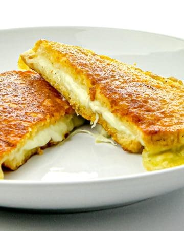Two halves of a crispy, golden grilled cheese sandwich with melted cheese oozing out on a white plate.
