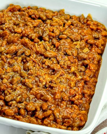 Baked beans in a white square dish on a patterned cloth with white background.