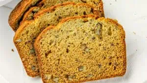 Four slices of nut-studded banana bread on white surface.