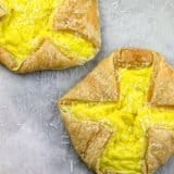Two puff pastry tarts filled with scrambled eggs and sprinkled with grated cheese on parchment paper.