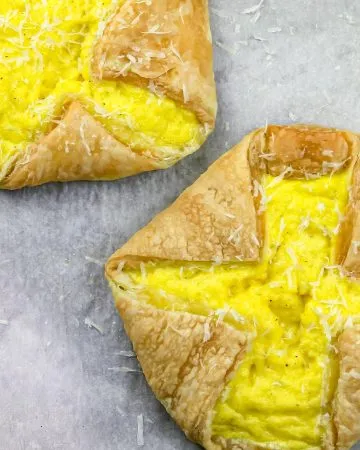 Two puff pastry tarts filled with scrambled eggs and sprinkled with grated cheese on parchment paper.