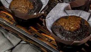Two chocolate muffins in brown paper wrappers placed in a woven basket.
