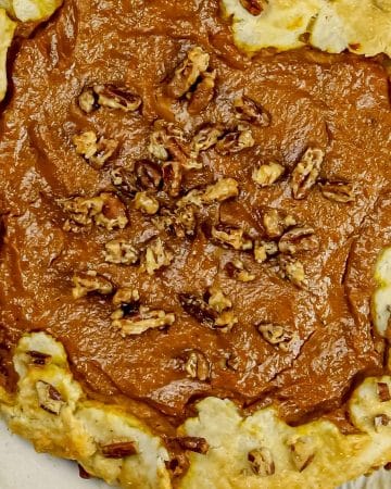 Rustic pumpkin pie galette with golden crust and pecans on parchment paper.