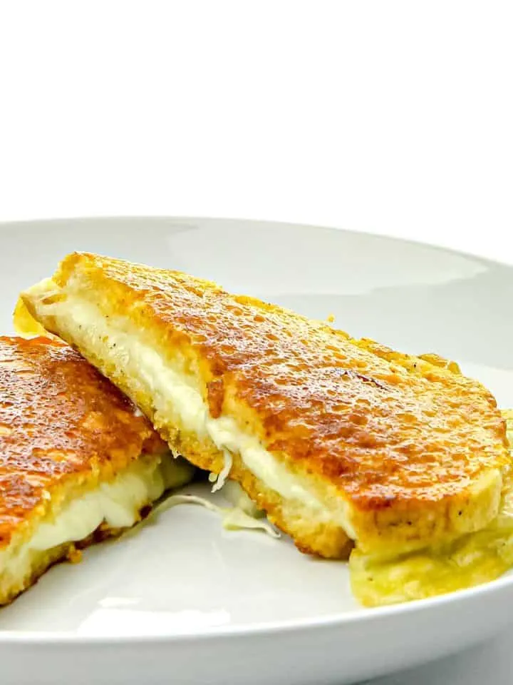 Golden grilled cheese sandwich cut in half with melted cheese oozing, served on a white plate.