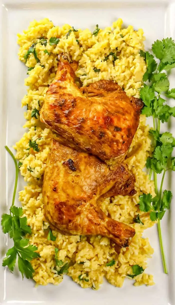 Two roasted chicken leg quarters on yellow rice garnished with cilantro on a rectangular white plate.