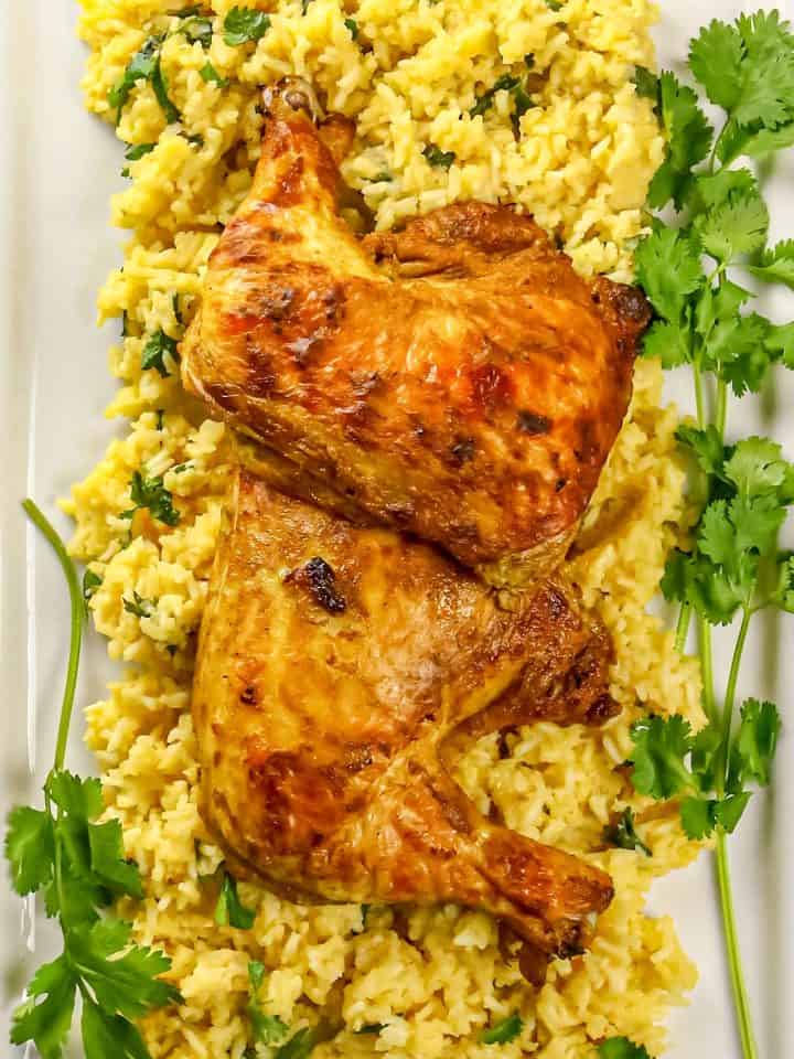Two roasted chicken leg quarters on yellow rice garnished with cilantro on a rectangular white plate.