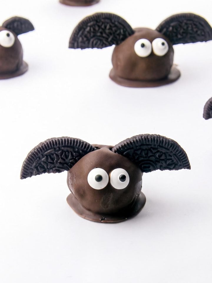 Chocolate balls decorated as bats with Oreo cookie wings and candy eyes on a white background.