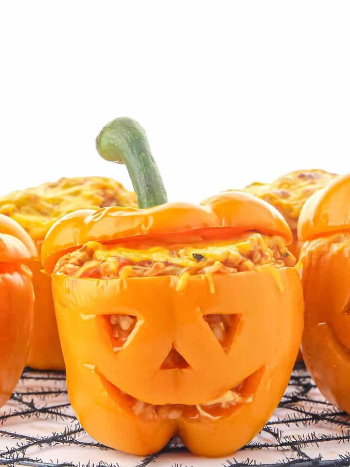 Orange bell peppers carved like jack-o'-lanterns, stuffed with a cheesy rice mixture, resting on a black spider web mat.