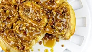 Sticky caramel pecan cinnamon rolls on a white plate with caramel sauce dripping.
