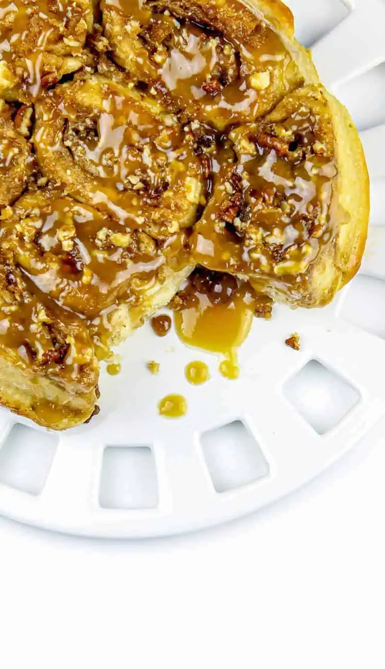 Sticky caramel pecan cinnamon rolls on a white plate with caramel sauce dripping on the side.