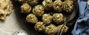 Herbed meatballs in a black pan with flatbread on a beige cloth and a blue napkin nearby.