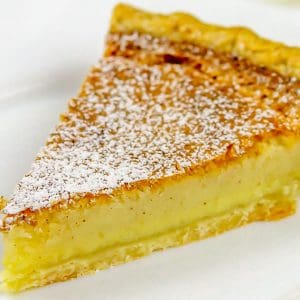Slice of custard pie with powdered sugar on top on a white plate.
