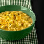 Green bowl filled with creamy macaroni and cheese garnished with herbs, placed on a green and white checkered cloth.