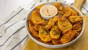 Crispy fried potato wedges sprinkled with herbs served with a creamy dipping sauce in a white bowl on a wooden board and striped cloth.