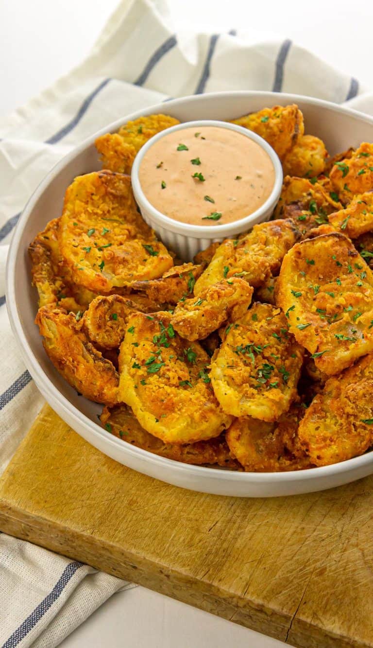 Crispy potato wedges garnished with herbs served with a creamy dipping sauce in a white bowl on a wooden board.