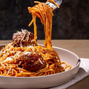 Spaghetti with meatballs topped with grated cheese in a beige bowl, with fork lifting a portion of pasta.