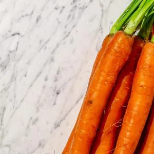 Bunch of fresh carrots with green tops on a white marble surface.