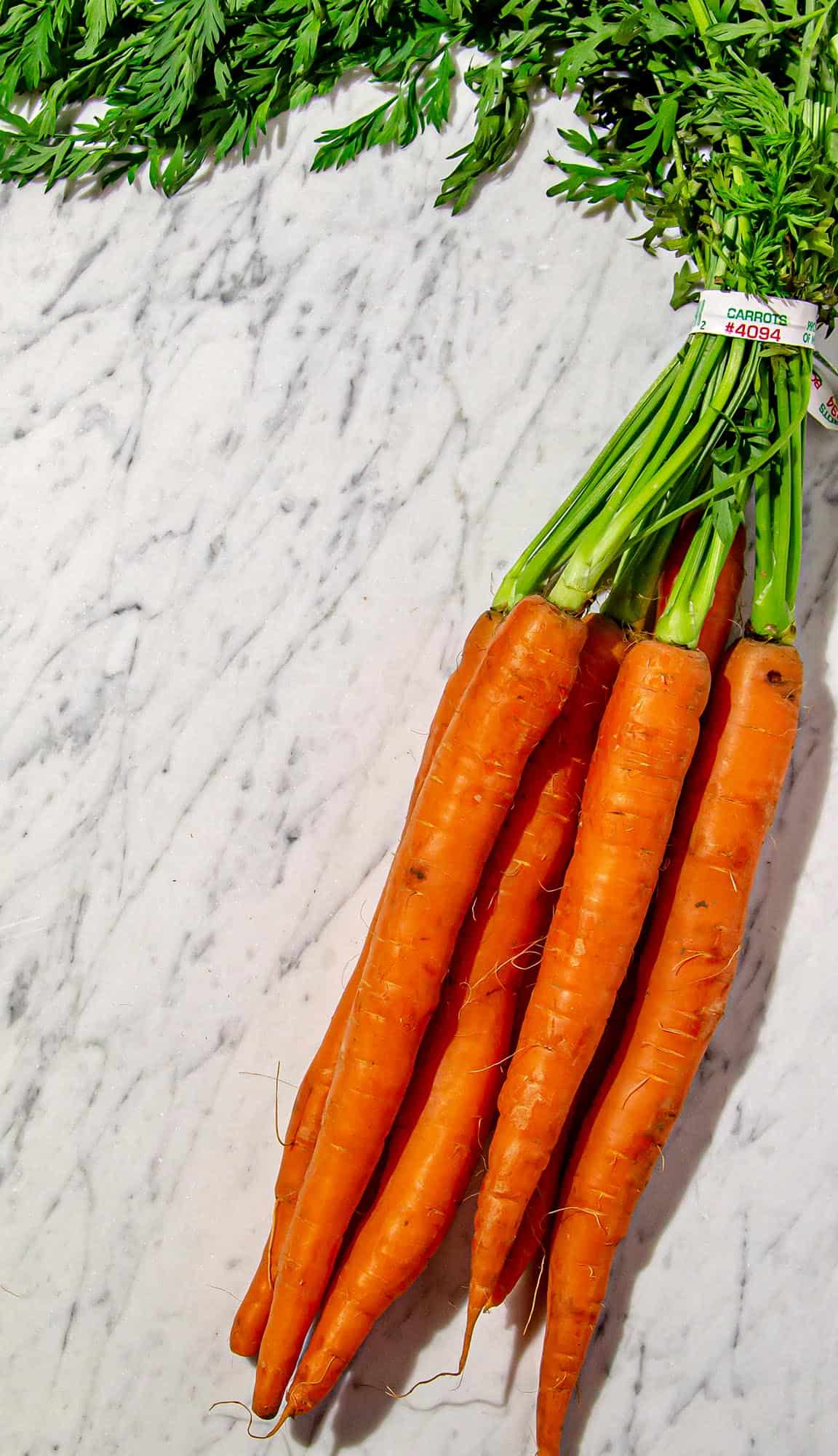 Bunch of six fresh orange carrots with green tops on a white marble surface.