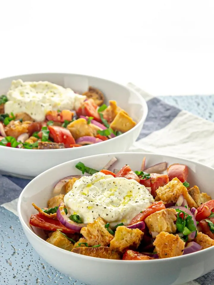 Two bowls of pita bread salad with tomatoes, red onions, herbs, topped with dollops of seasoned ricotta.