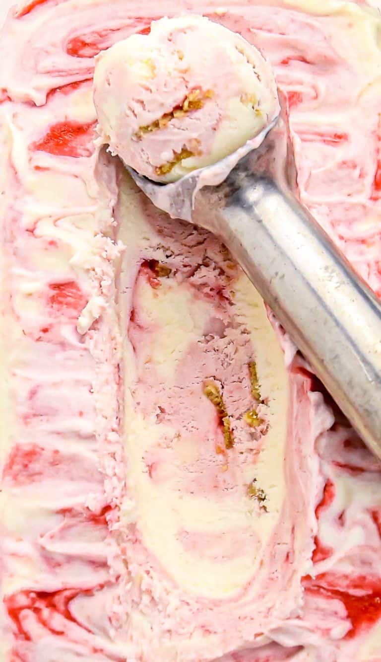 Scoop of pink and white swirled ice cream with red fruit sauce and nuts in a metal ice cream scoop.