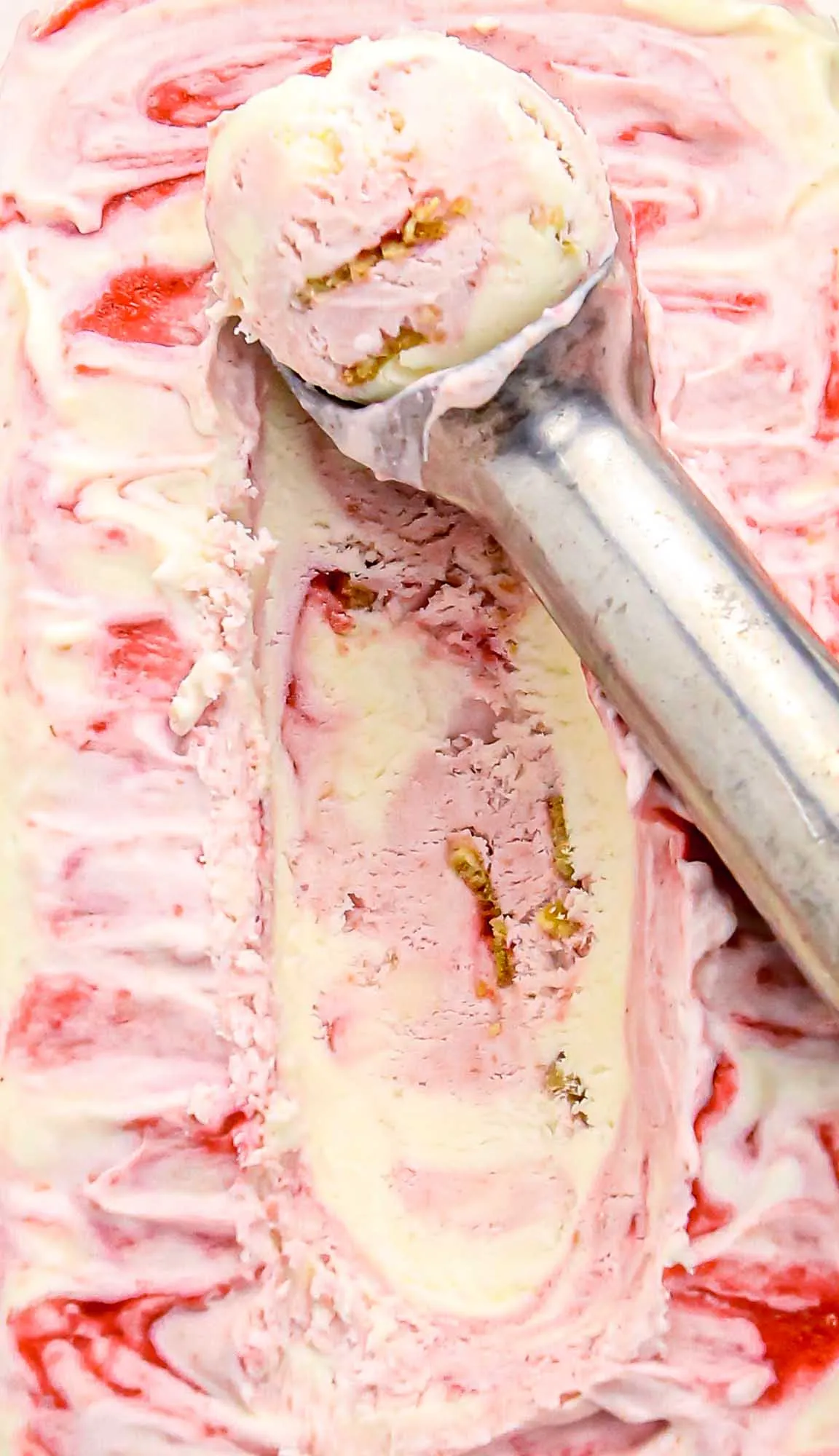 Scoop of pink and white swirled ice cream with red fruit sauce and nuts in a metal ice cream scoop.
