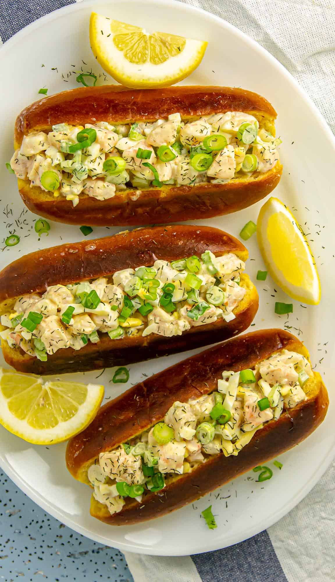 Three creamy chicken salad sandwiches garnished with green onions and dill on a white plate with lemon wedges.
