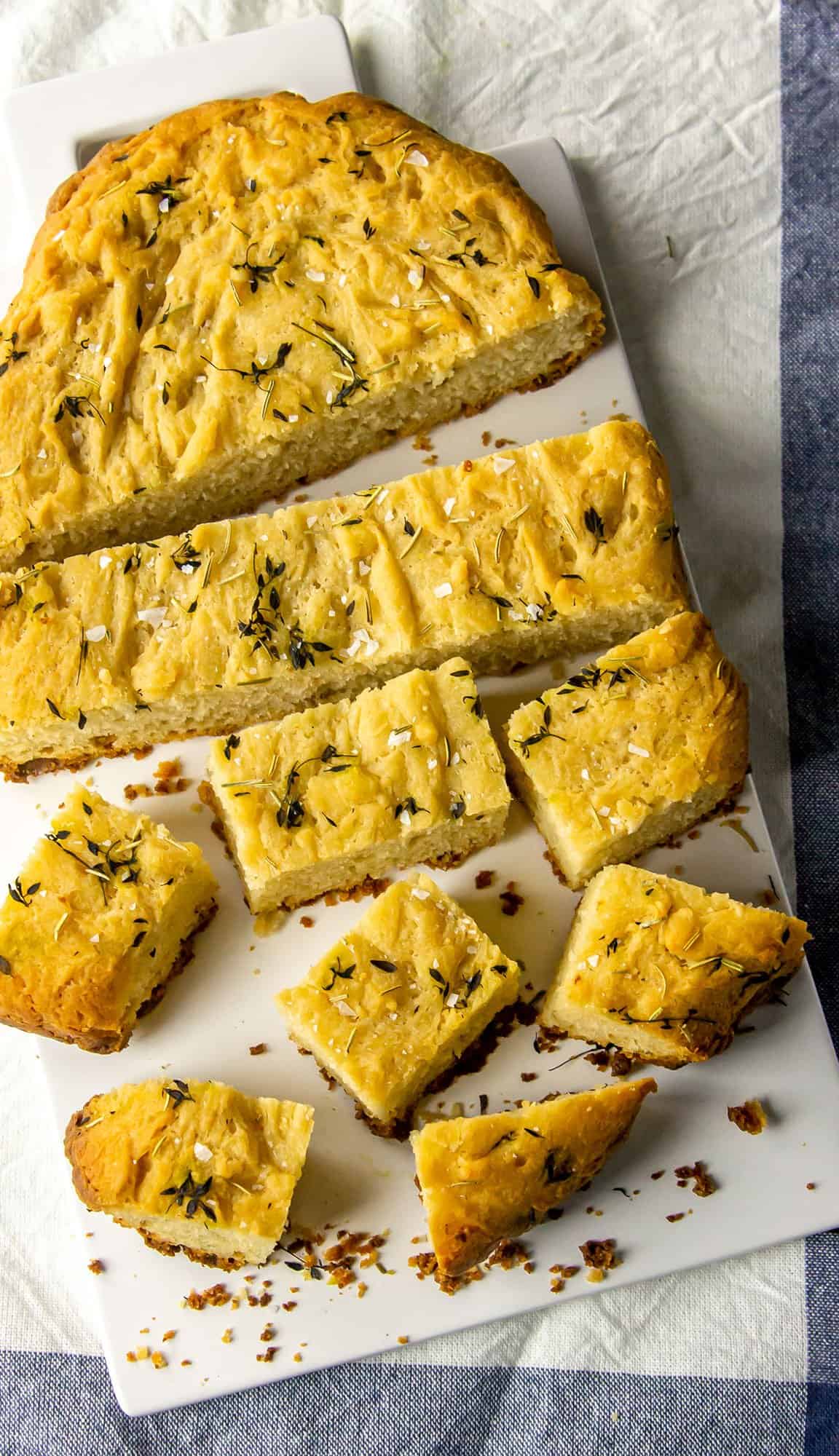 Herb-topped focaccia bread sliced into various shapes on a white rectangular plate.
