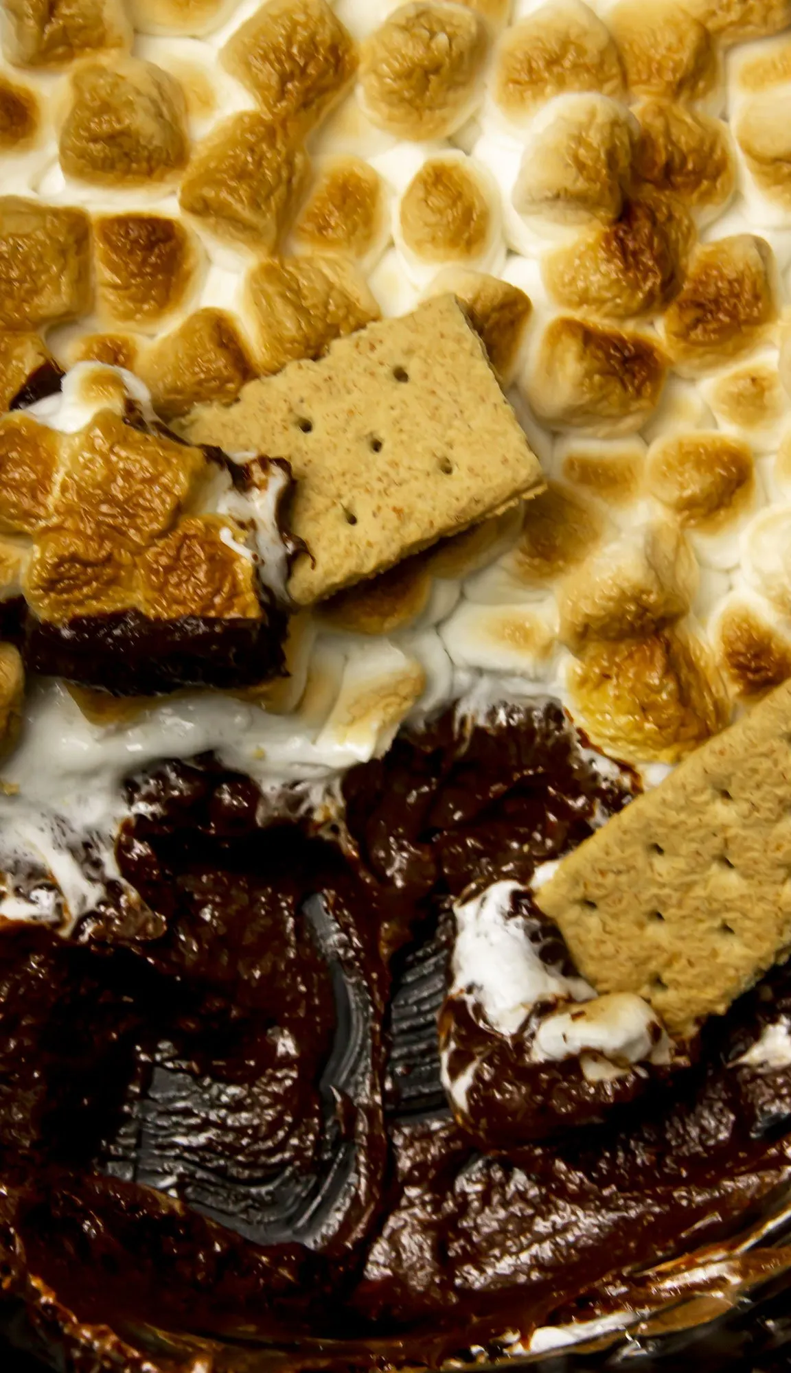 Toasted marshmallows, melted chocolate, and graham crackers in a skillet, resembling a gooey s'mores dessert.
