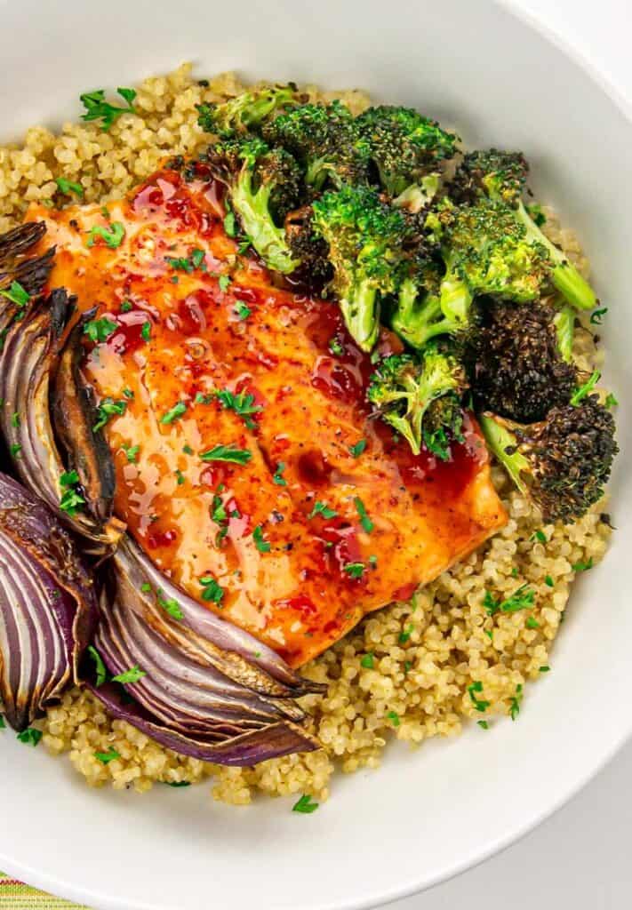 Salmon glazed with sauce, roasted broccoli, red onion, and quinoa garnished with parsley in a white bowl.