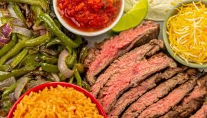 Air fryer steak fajitas presented with cooked peppers and onions, cheese, sour cream, and Spanish rice