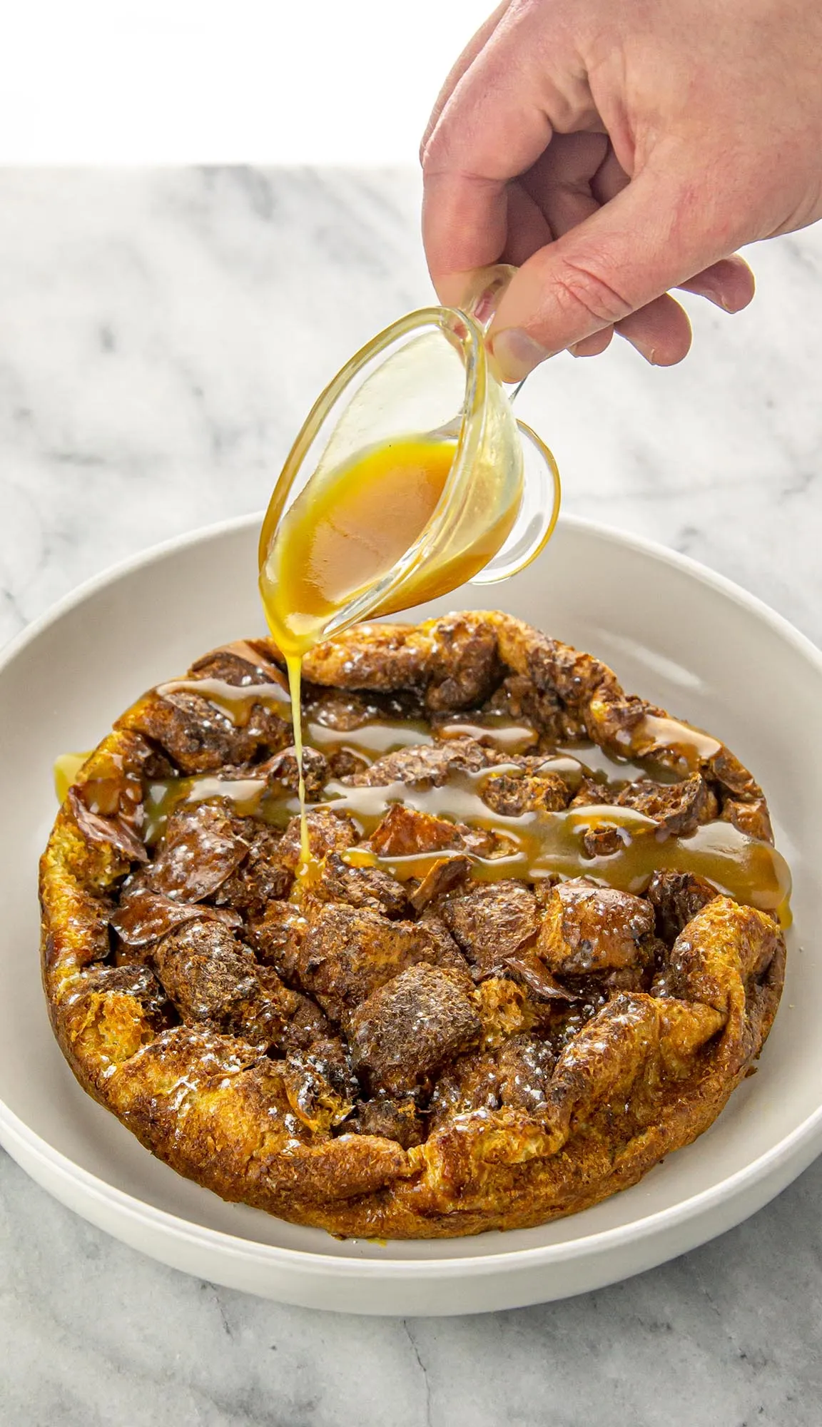 Bread pudding with a hand pouring praline sauce over the top