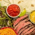 Air fryer steak fajitas presented with cooked peppers and onions, cheese, sour cream, and Spanish rice