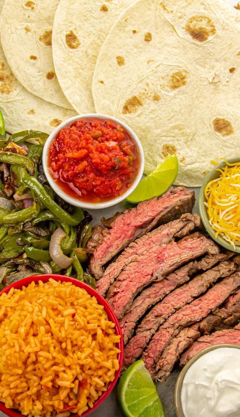 Air fryer steak fajitas presented with cooked peppers and onions, cheese, sour cream, and Spanish rice