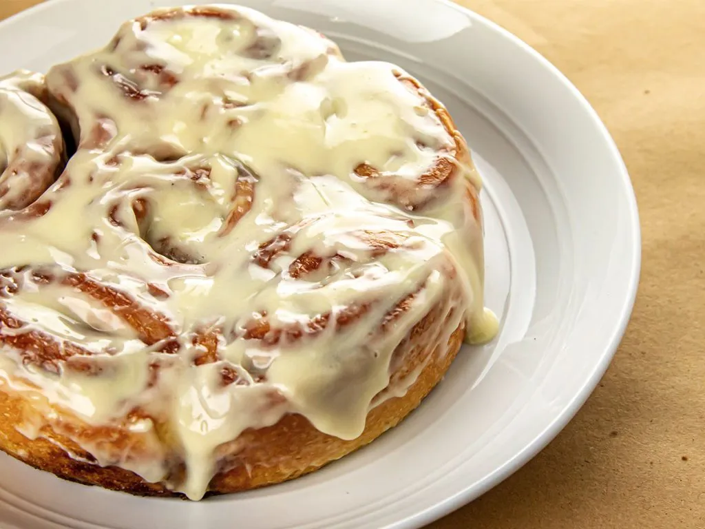 A plate of cinnamon rolls covered with meltng cream cheese frosting