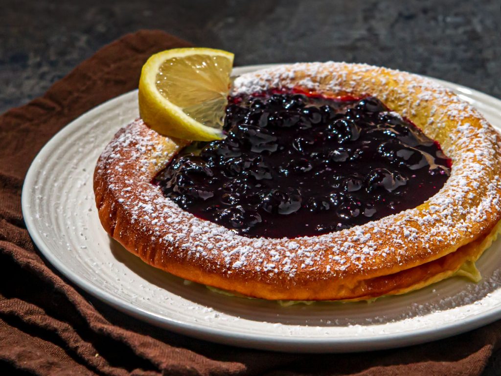 A dutch baby pancake served with a blueberry compote in the center, dusted with powdered sugar and a lemon wedge on the side