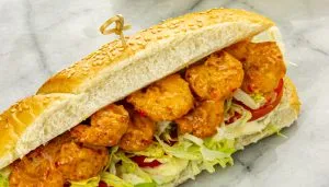 Two po' boy sandwiches with breaded shrimp, sliced tomato, lettuce and mayo