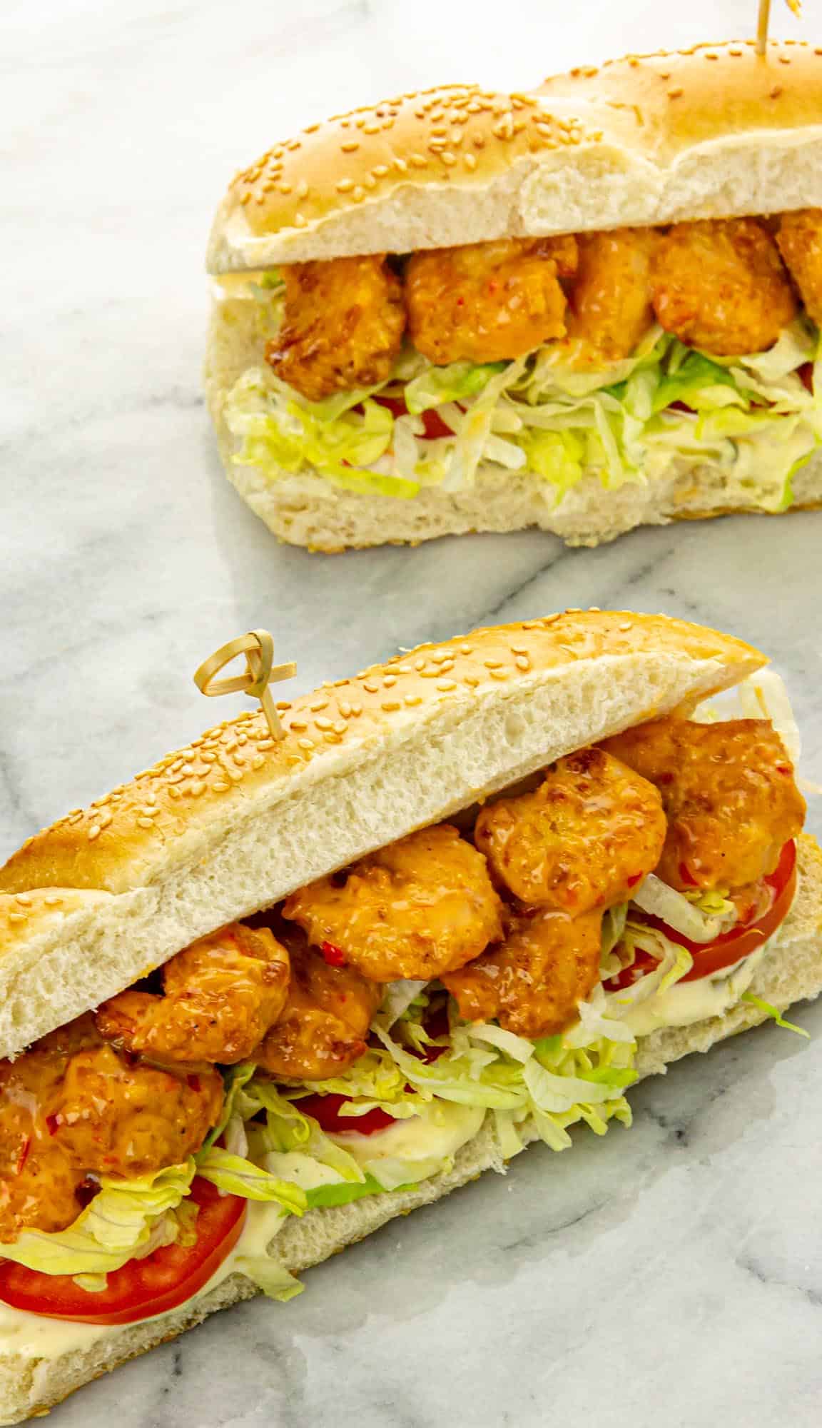 Two po' boy sandwiches with breaded shrimp, sliced tomato, lettuce and mayo
