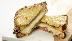 Sliced sandwich with melty cheese oozing out with sliced ham and broiled cheese on top