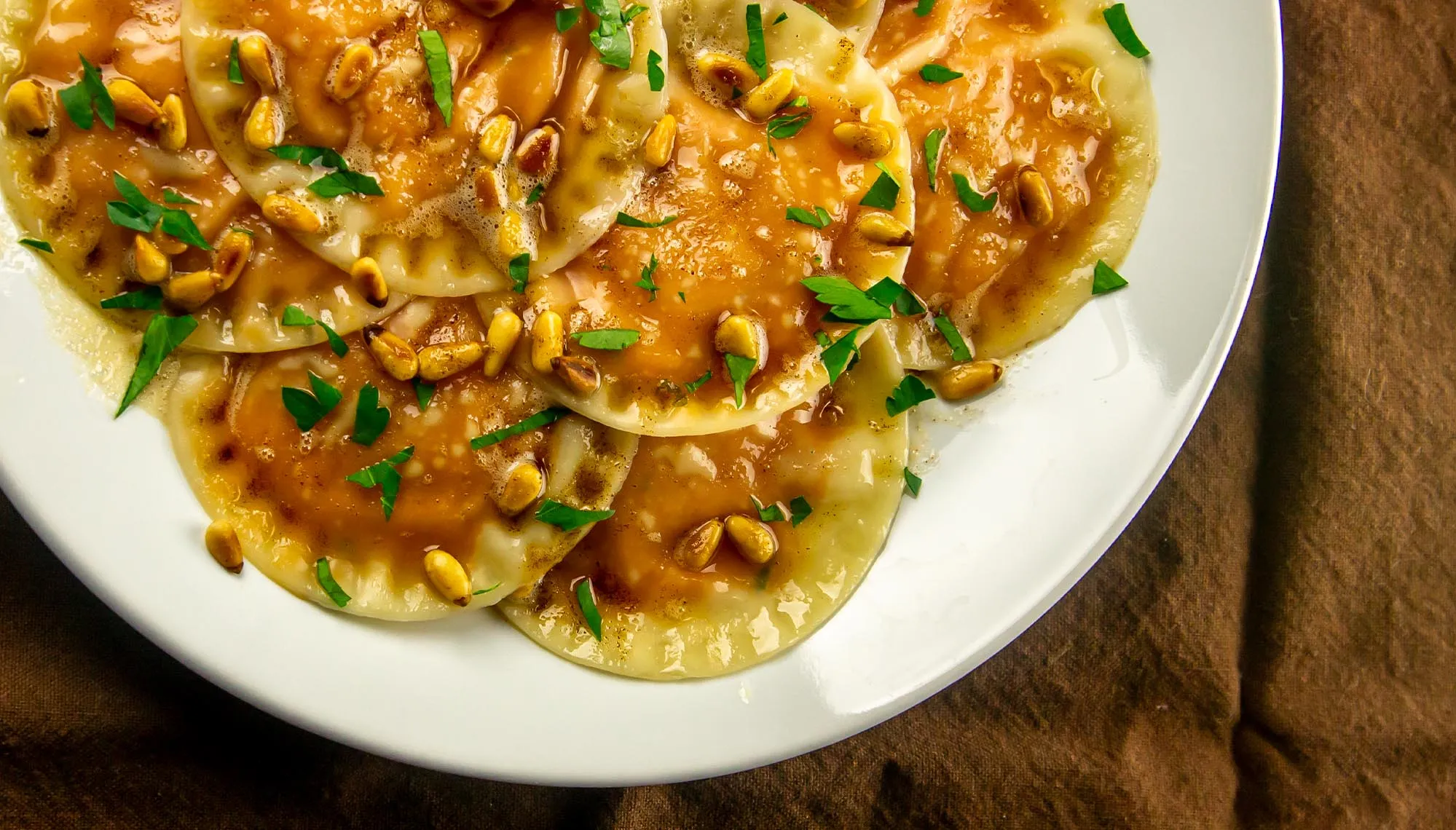 ravioli with sweet potato filling topped with a browned butter sauce and pine nuts