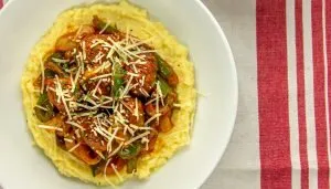 Creamy polenta topped with cooked chicken, green bell peppers, onions, tomato sauce, and shredded Parmesan cheese in a white bowl.