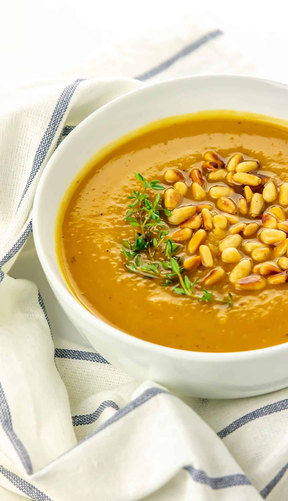 bowl of butternut squash soup with pine nuts and fresh thyme sprigs