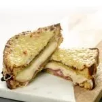 Sliced sandwich with melty cheese oozing out with sliced ham and broiled cheese on top
