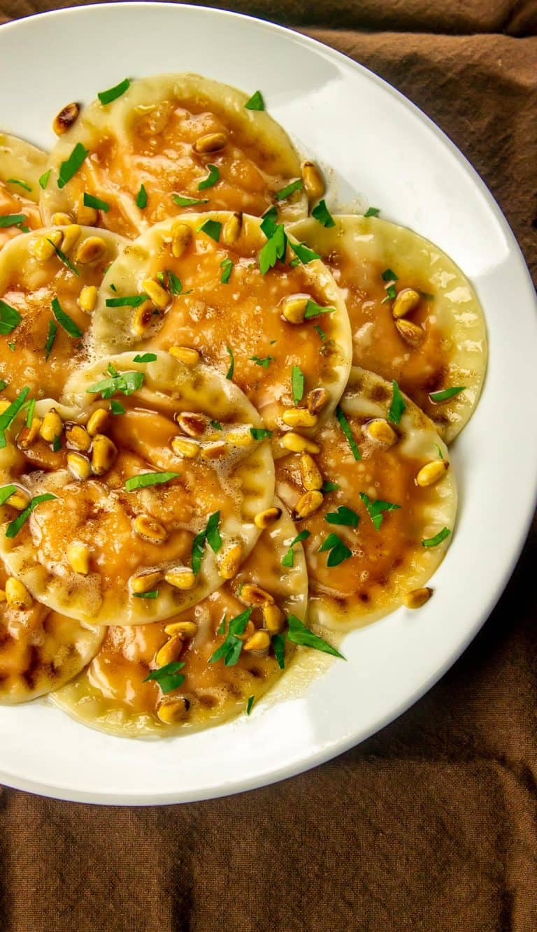 ravioli with sweet potato filling topped with a browned butter sauce and pine nuts