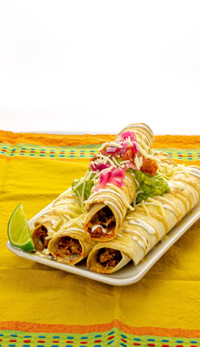 Chicken taquitos with pickled onion, guacamole, and sour cream on top