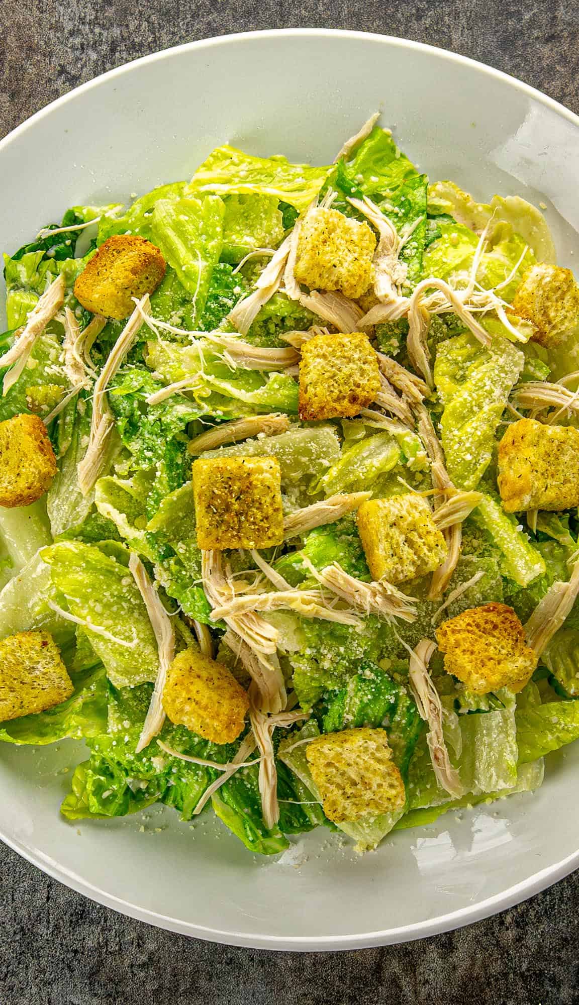Caesar salad with romaine lettuce, shredded chicken, croutons, and grated Parmesan cheese on a white plate.