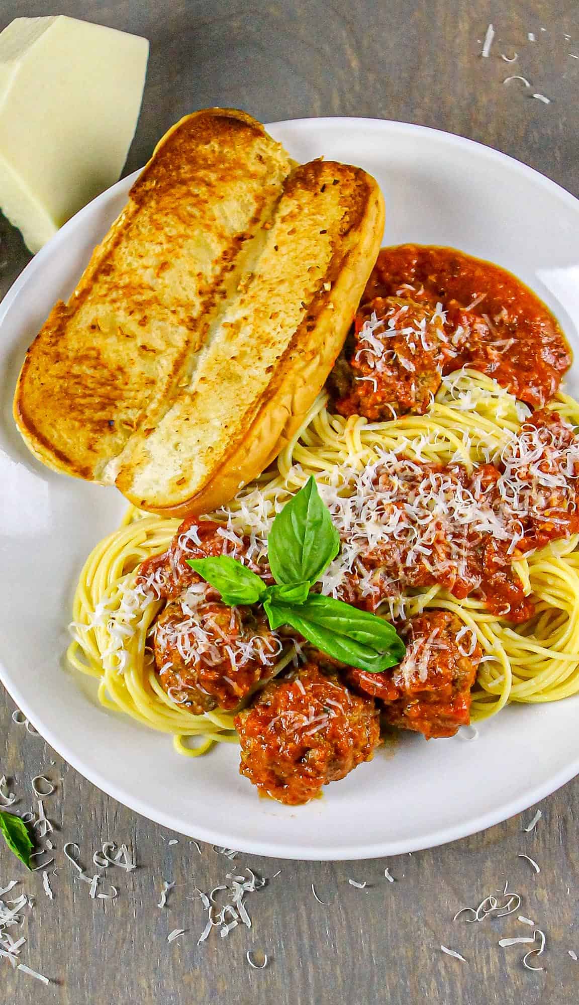 Spaghetti with meatballs in marinara sauce, grated cheese, basil garnish, and two slices of garlic bread on a white plate.