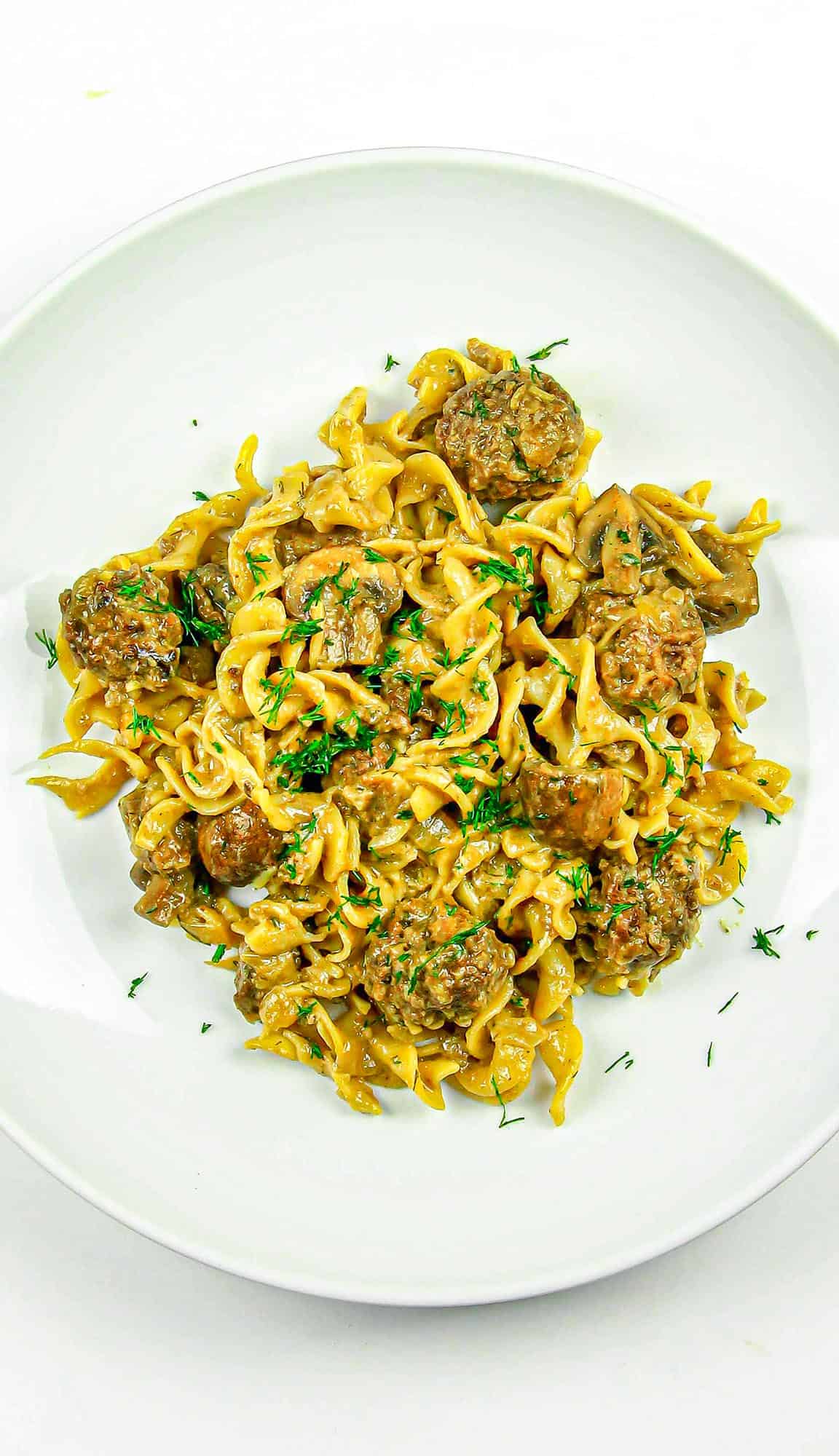 Beef stroganoff with egg noodles, mushrooms, and fresh herbs on a white plate.