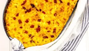 Baked macaroni and cheese casserole topped with crispy bacon bits in a black baking dish wrapped with a white and blue striped cloth.