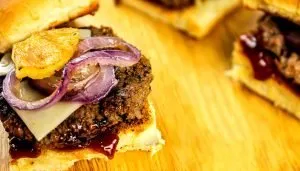 Grilled hamburger patty with melted cheese, grilled red onions, pineapple slice, and barbecue sauce on a toasted bun.