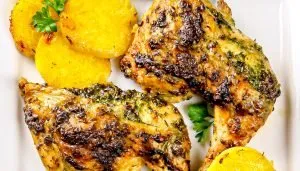 Grilled herb-marinated chicken thighs served with rounds of roasted yellow potatoes and parsley garnish on a white plate.